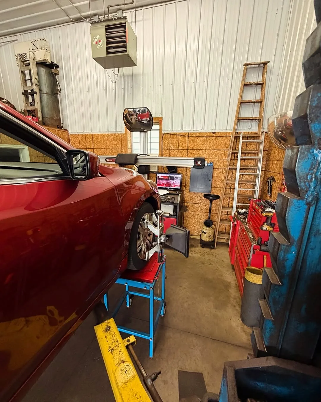 A red car on the alignment rack in the shop, a sensor clamped to its front wheel